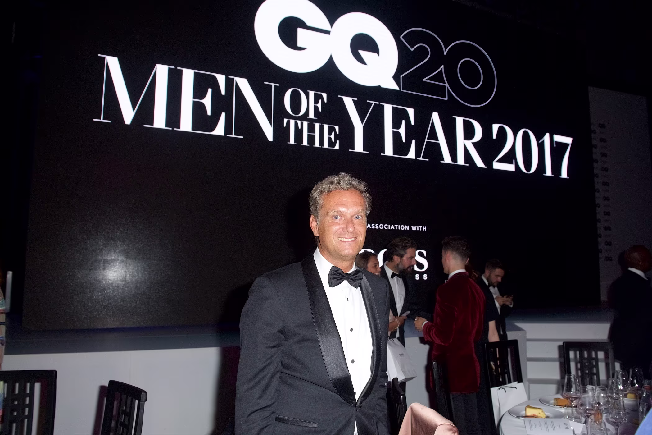 Stephan Born in a tuxedo poses in front of a GQ Men of the Year sign.