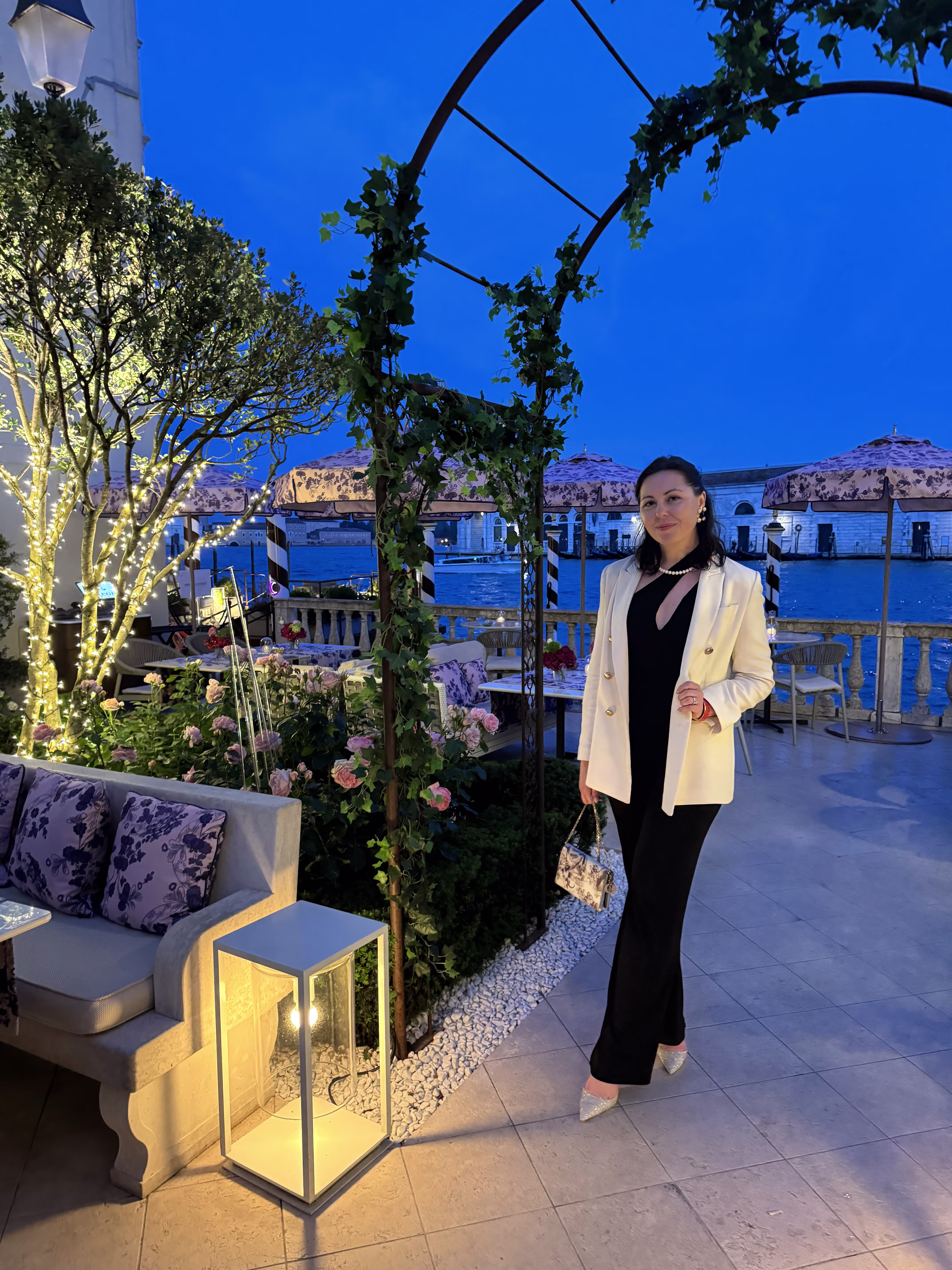 Kristina standing on a lit terrace near the water at night.