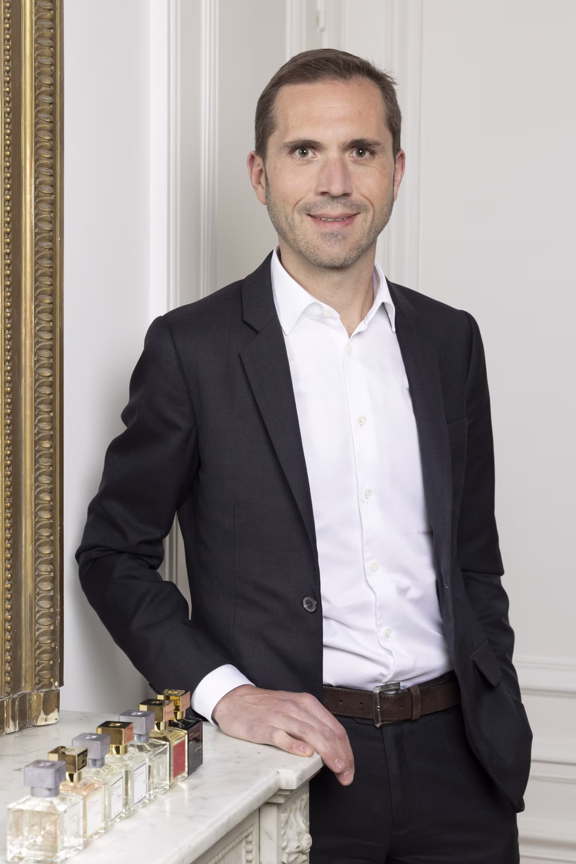 Headshot of Arnaud Sabadie in a white room next to a display of Maison Francis Kurkdjian fragrances.