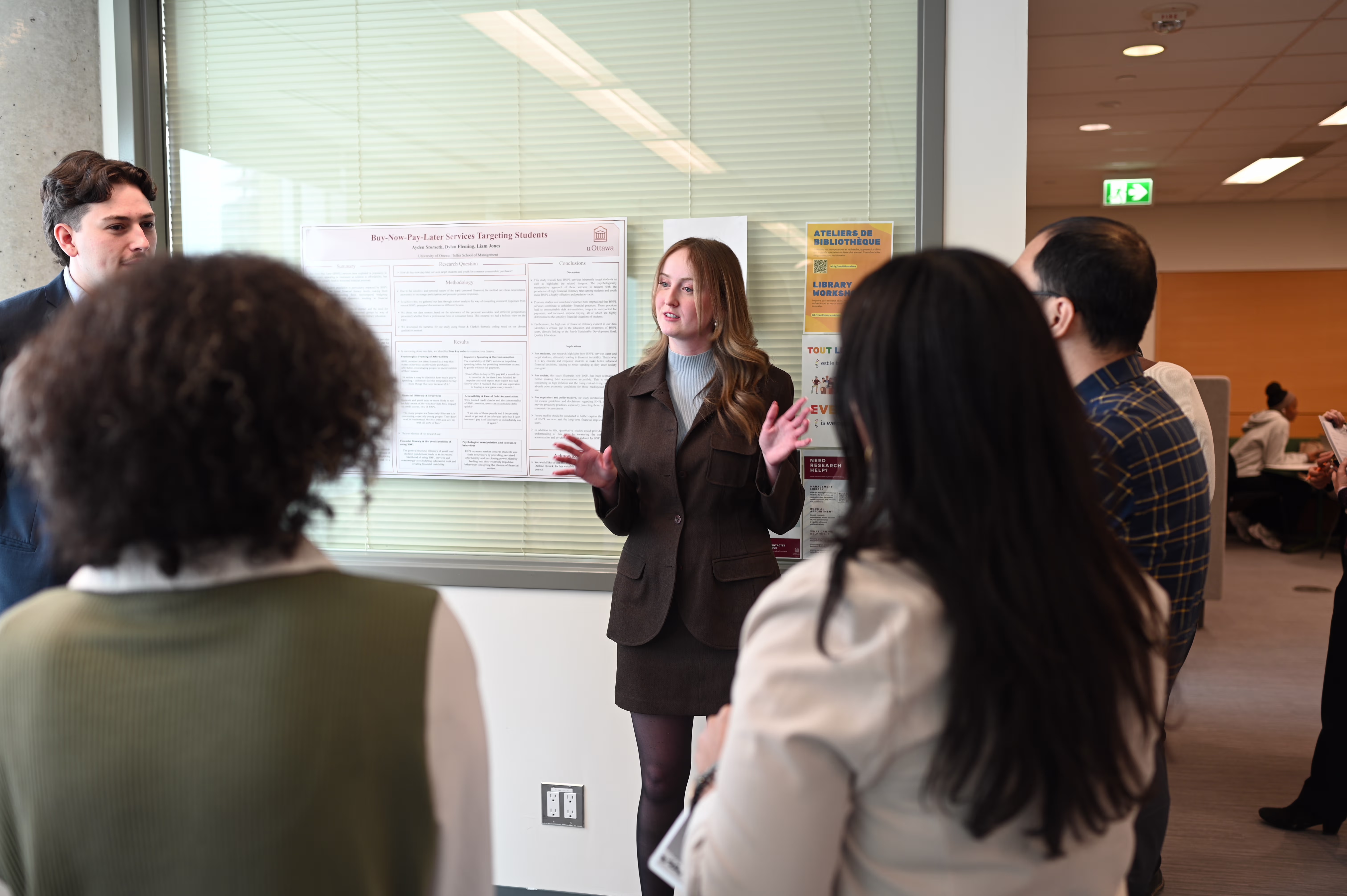A student presents her research poster to a group of students and visitors.