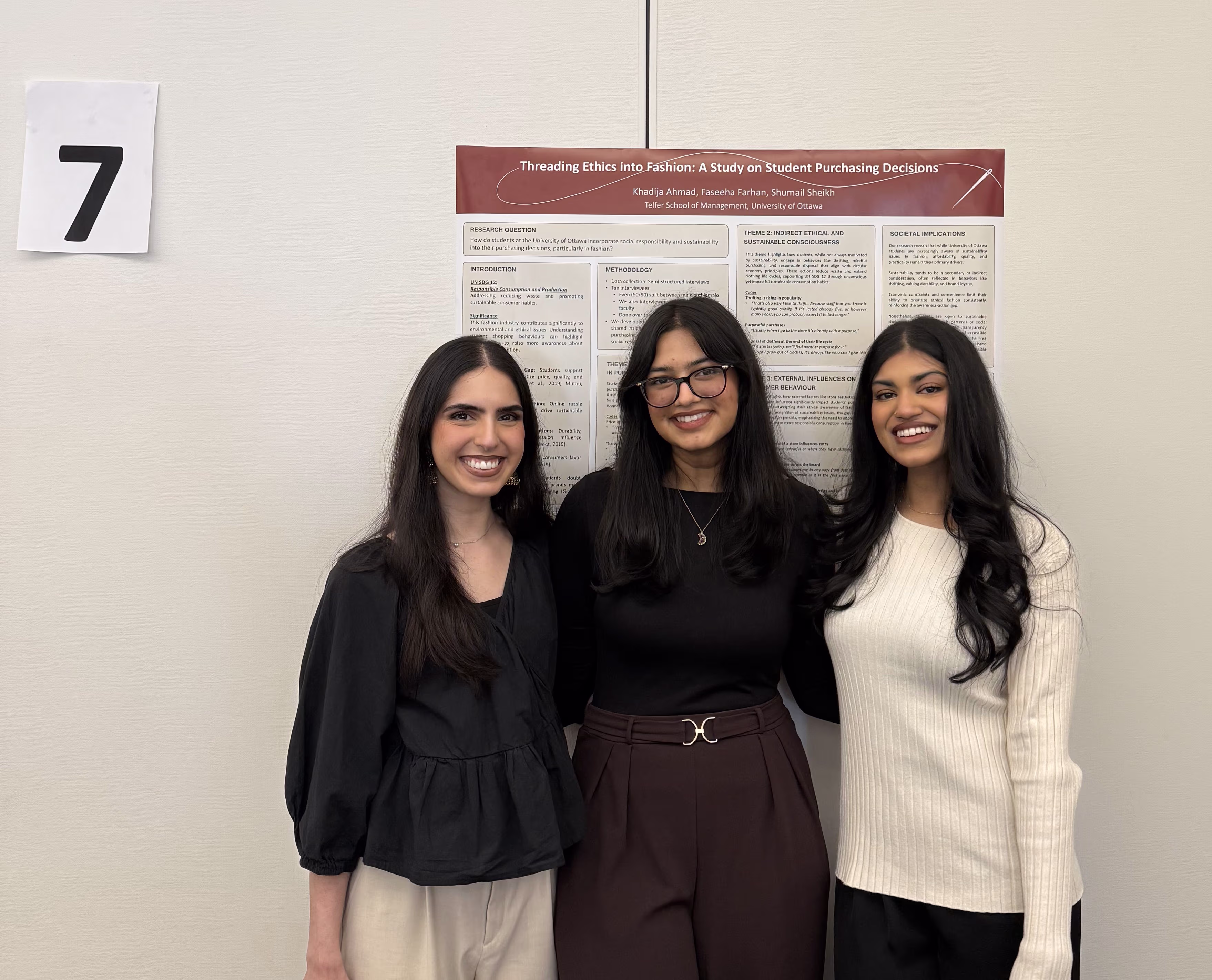 Three smiling students posing in front of their research poster