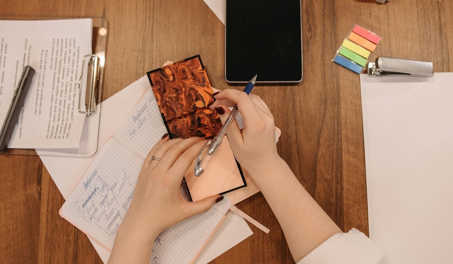 121 / 5,000 Les mains d'une femme sur le point d'écrire sur un bloc-notes sur un bureau contenant d'autres objets de bureau ; agrafeuse, papier, presse-papiers et IPAD