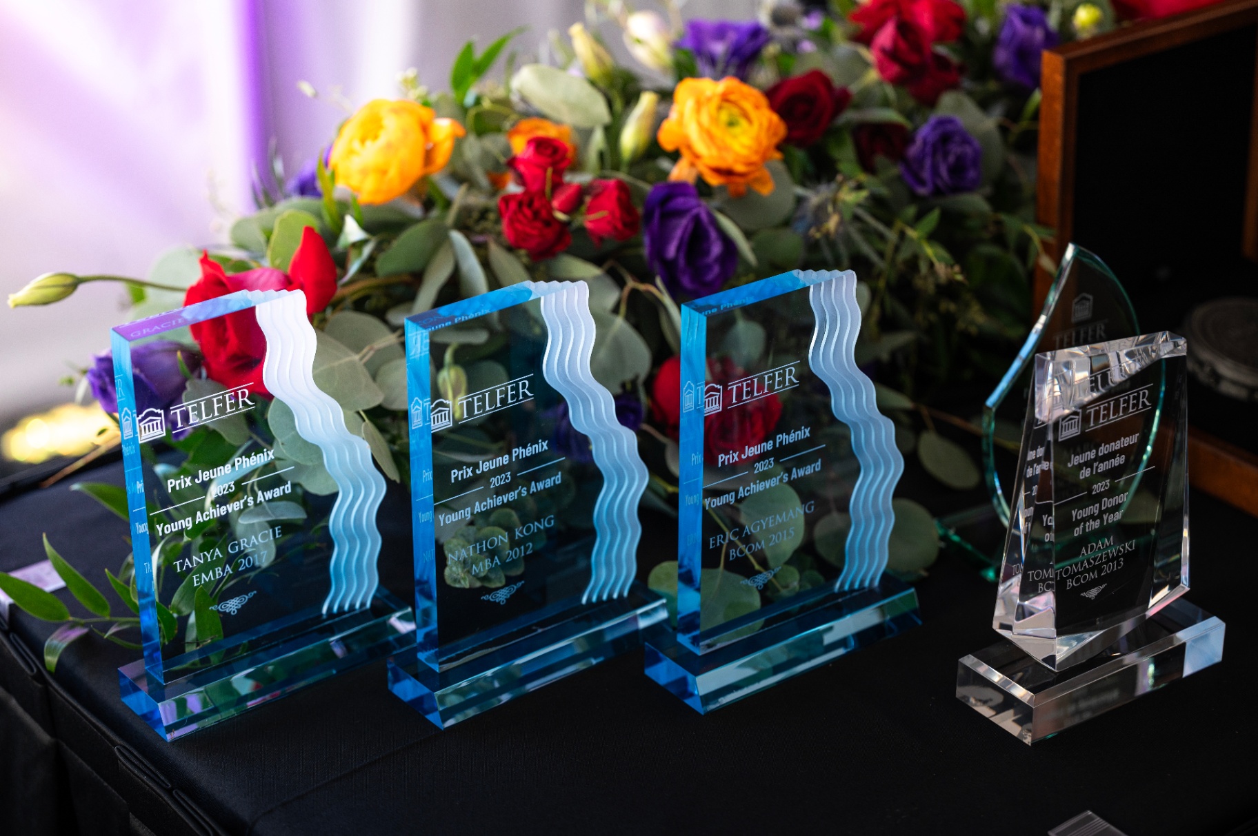Glass trophies of the Telfer Young Achievers’ Award displayed on a table with colorful flowers