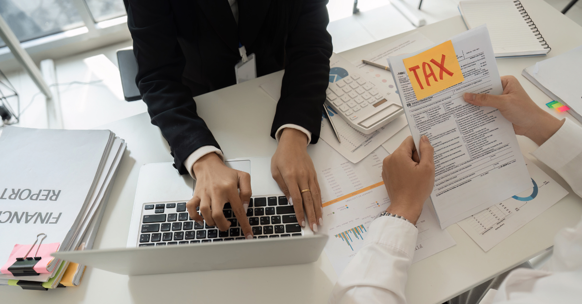 Deux personnes discutent, l'une tient des documents fiscaux et l'autre tape sur son ordinateur.