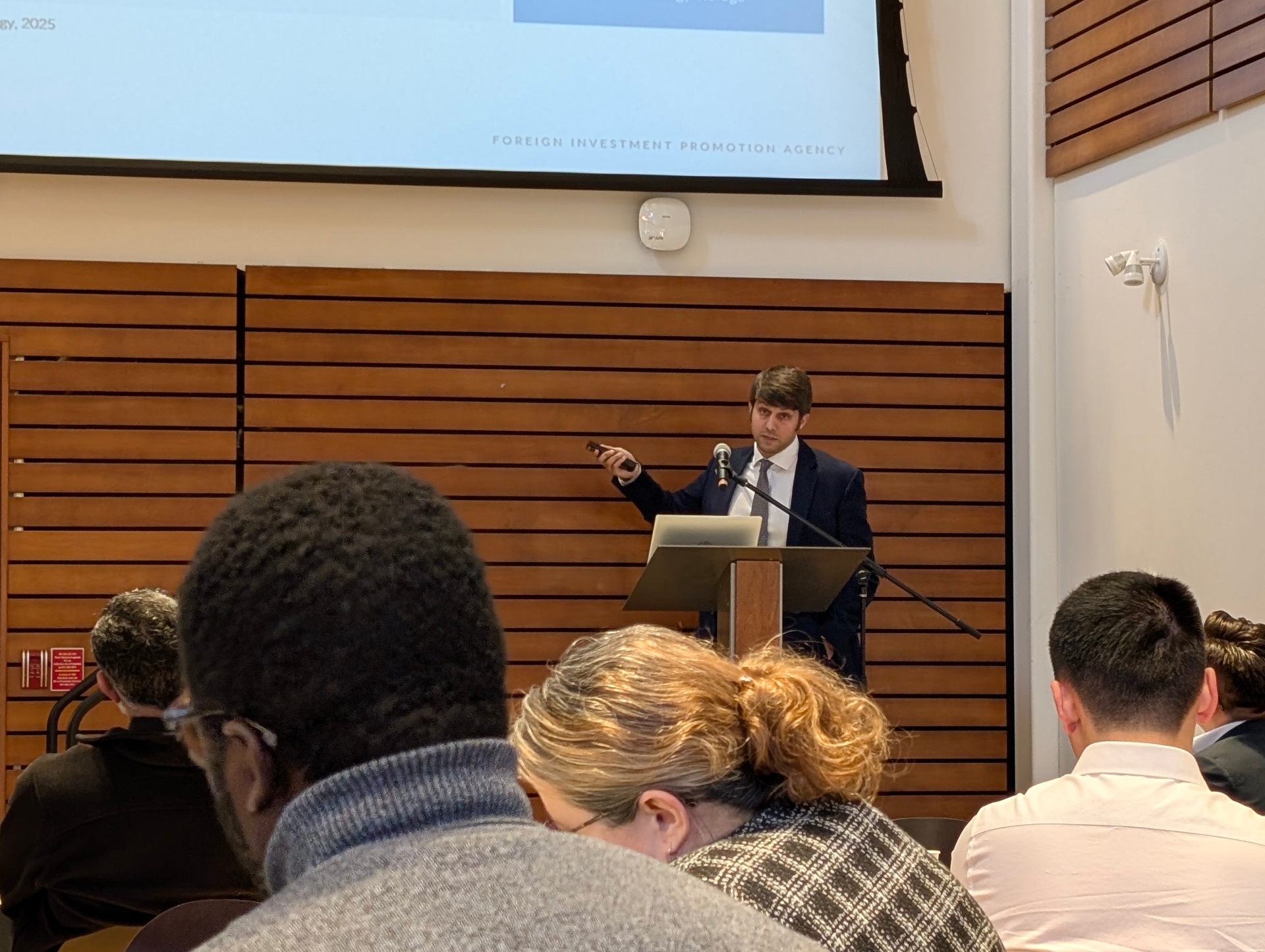 A presenter in a suit speaks at a podium while attendees watch. A slide from Chile’s foreign investment promotion agency is partially visible above.