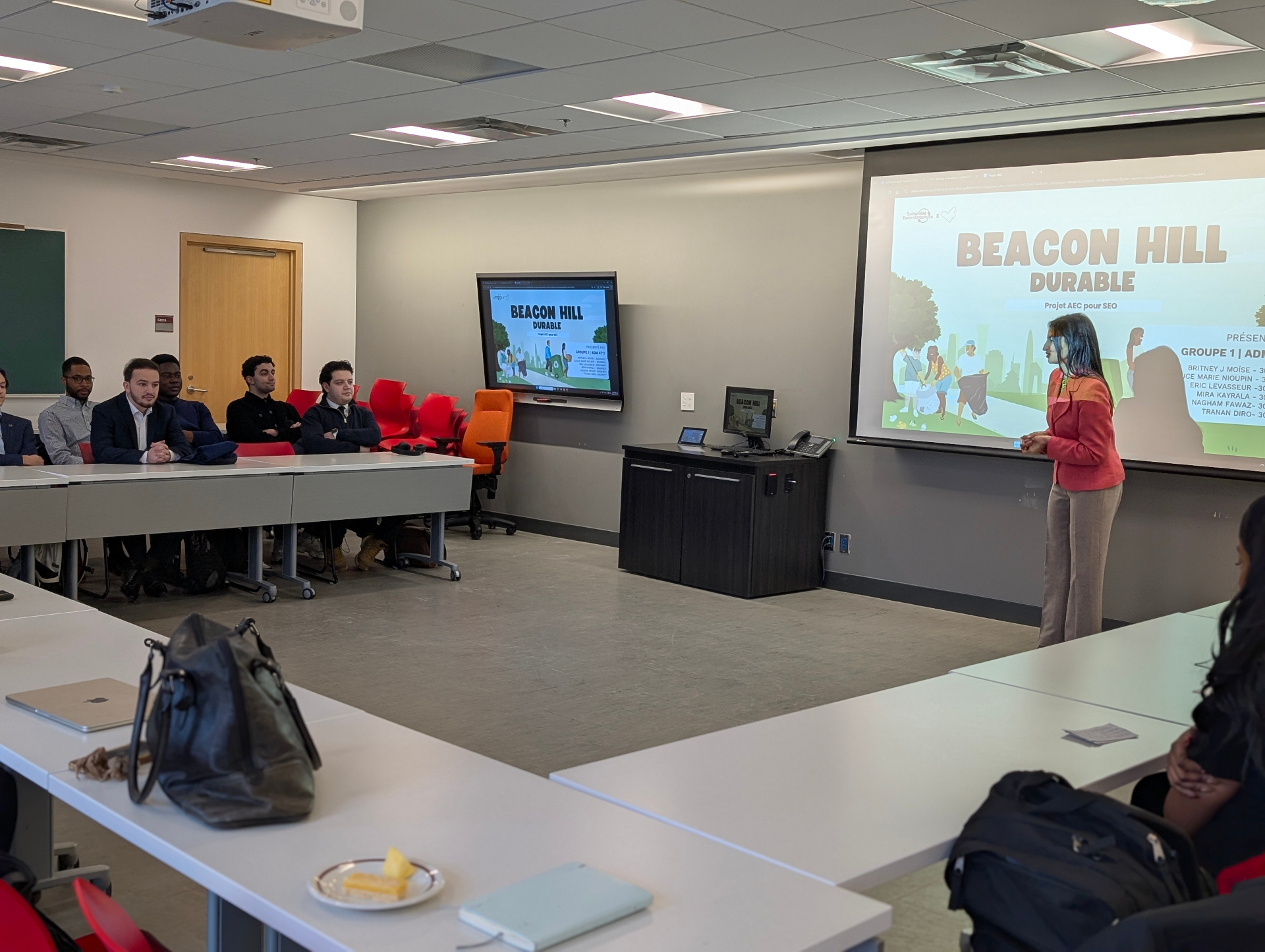 Professor Dorra Jlouli presents key sustainability challenges using a visual diagram on a projected slide, speaking to the audience during a final course presentation.