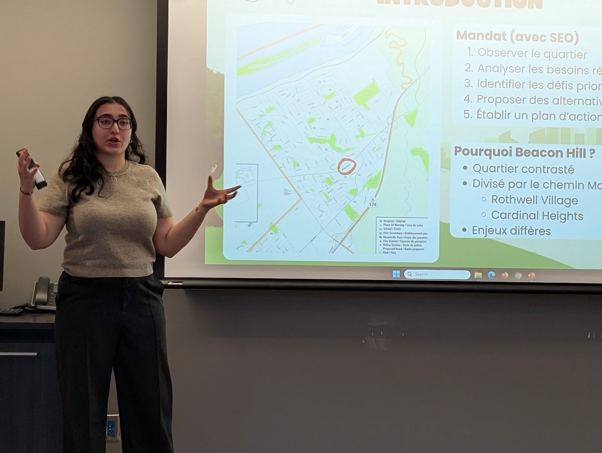 A student presents a neighborhood analysis using a projected map, gesturing toward the screen while explaining sustainability challenges and priorities.