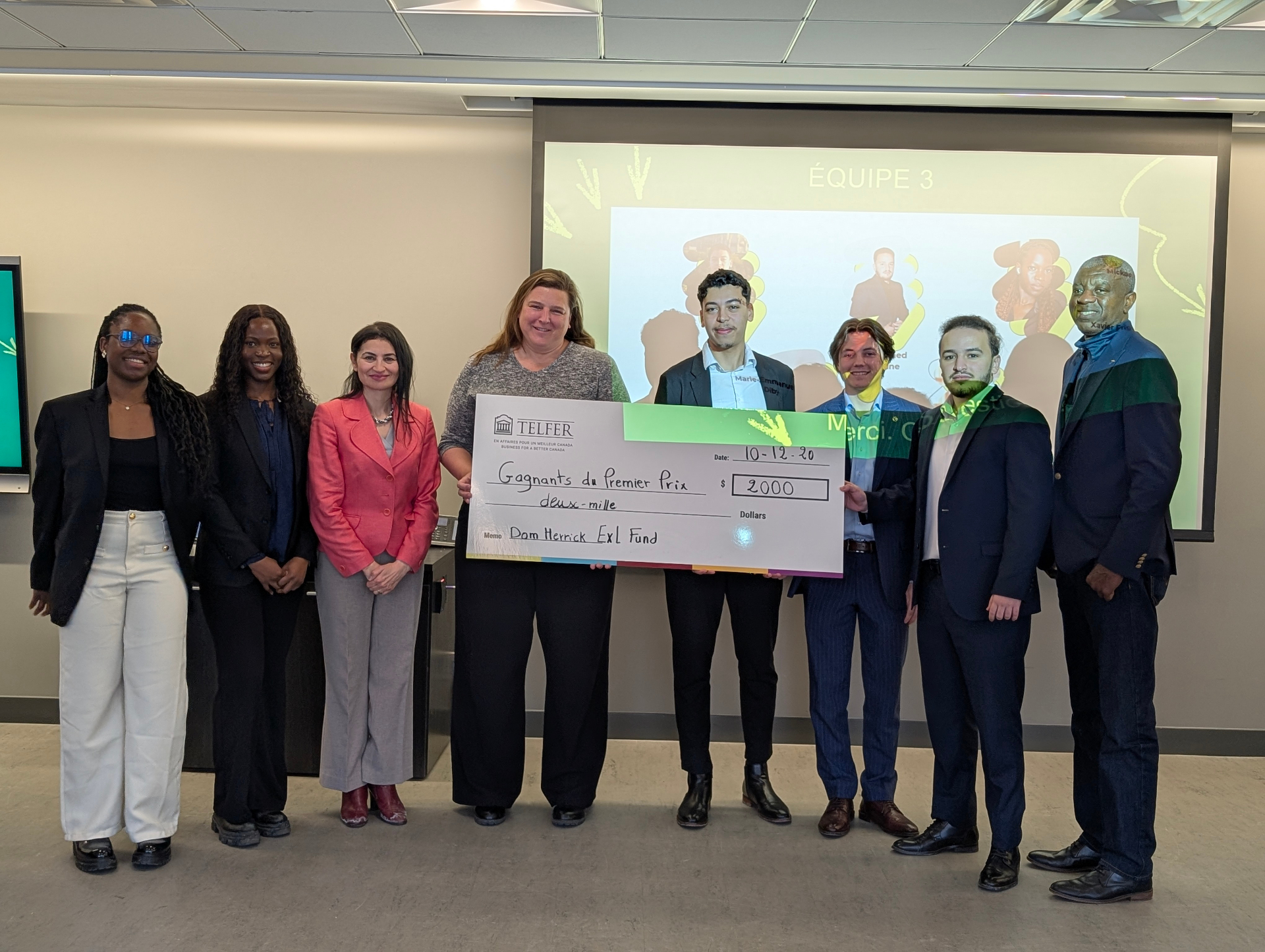 Group photo of students and faculty standing at the front of a classroom, holding a large cheque awarded for first place as part of an experiential learning project at the Telfer School of Management.