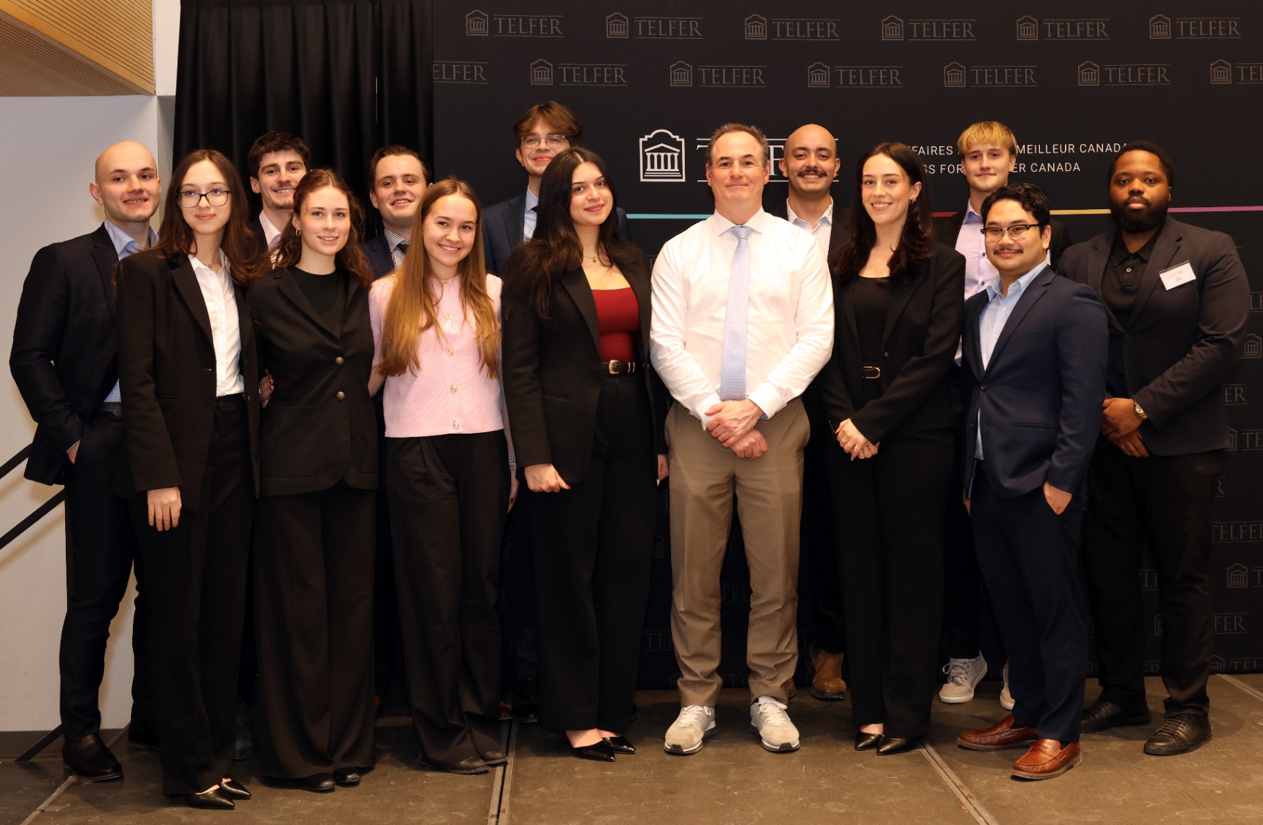 A group photo of Paul Halucha (center, in a white shirt) standing with members of the University of Ottawa Real Estate Club in front of a Telfer School of Management backdrop