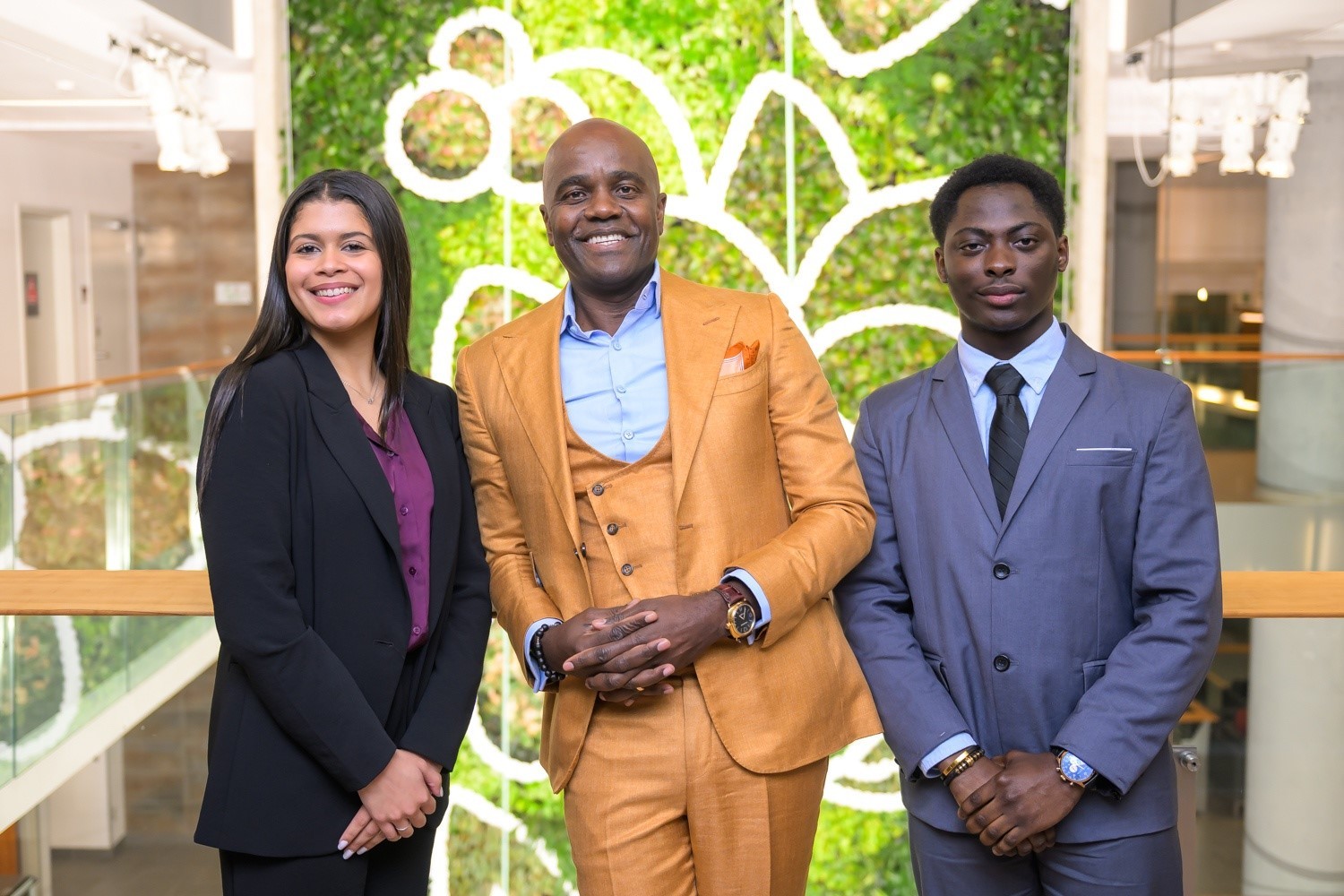 Wes Hall pose en costume jaune aux côtés d’Abigail et de Louis, boursière et boursier