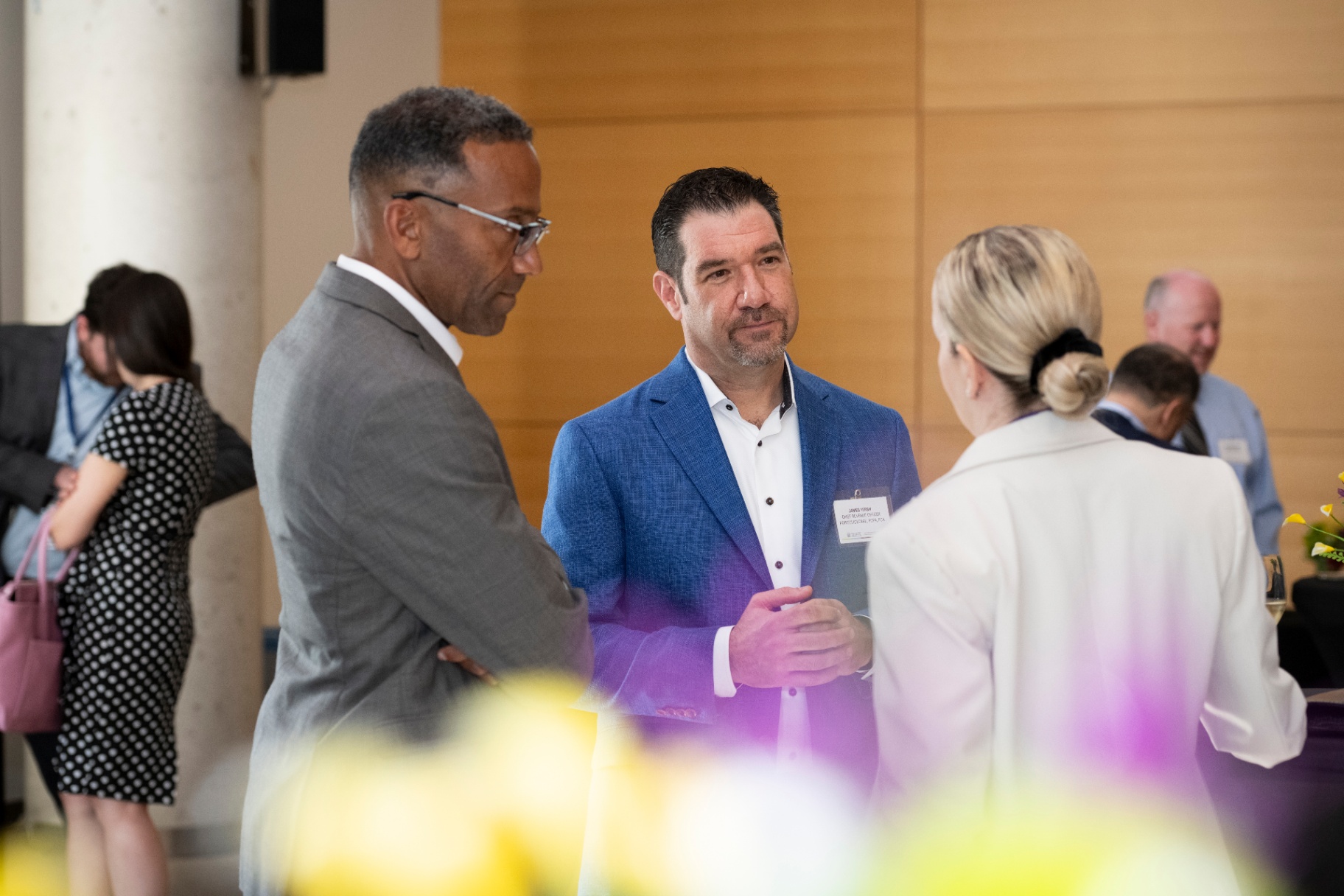 James Yersh, a dark-haired man in a blue suit, is in discussion with one man and one woman at a networking event.