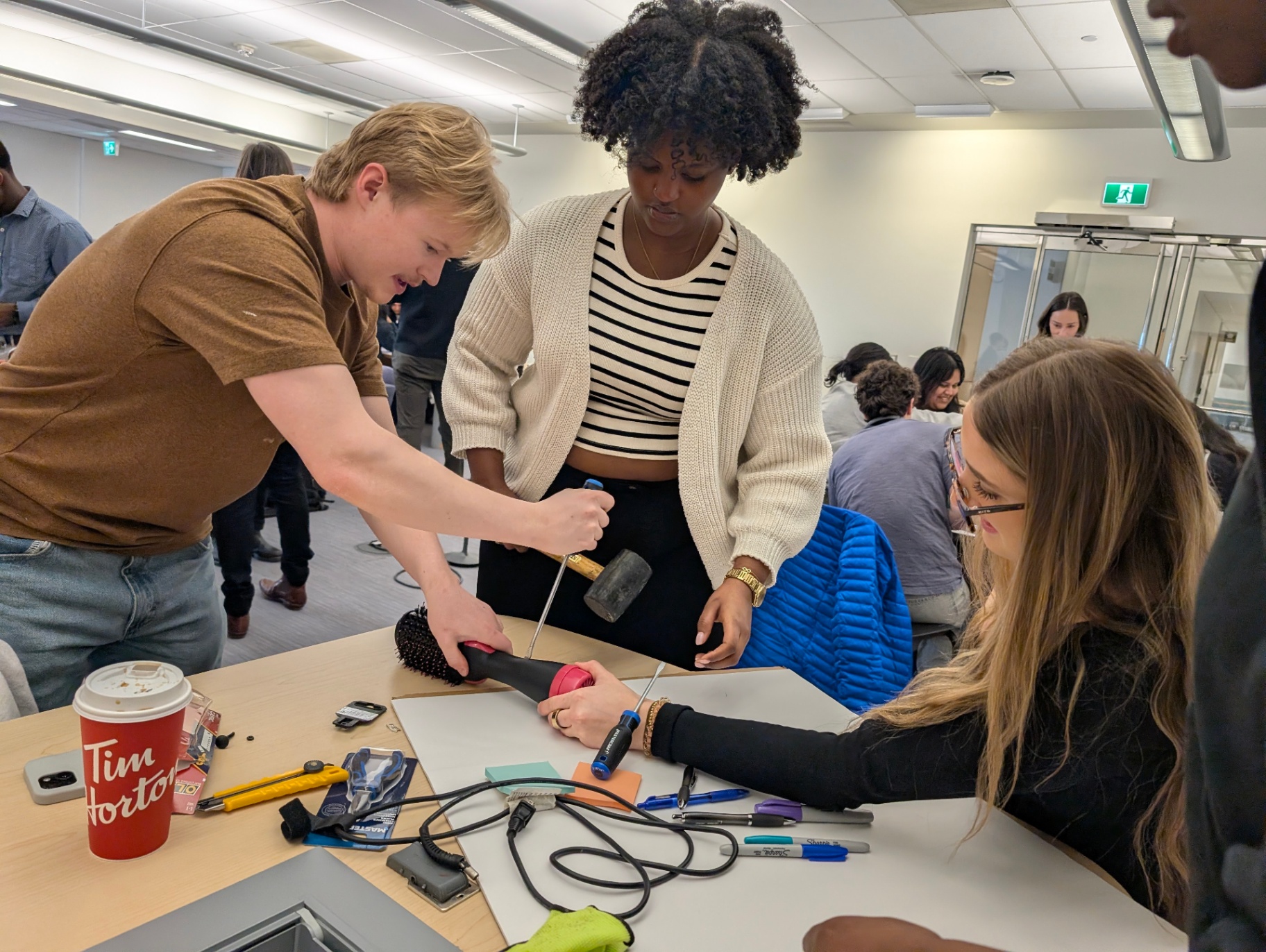 Students collaborate during a hands-on workshop, using tools to take apart an everyday object as part of a sustainability and design activity.