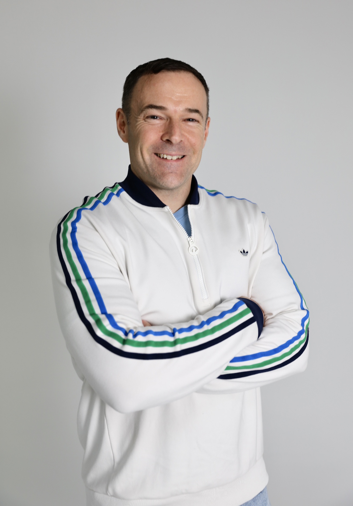 A portrait of Jonathan Cavalier, smiling and wearing an adidas jacket.