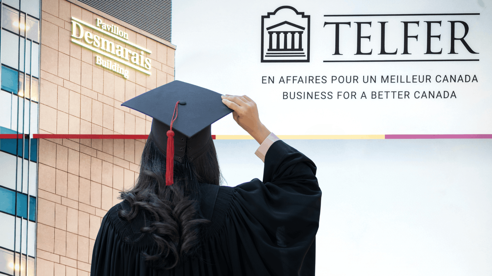 Graduate wearing a cap and gown posing in front of a Telfer School of Management backdrop during Convocation celebrations.