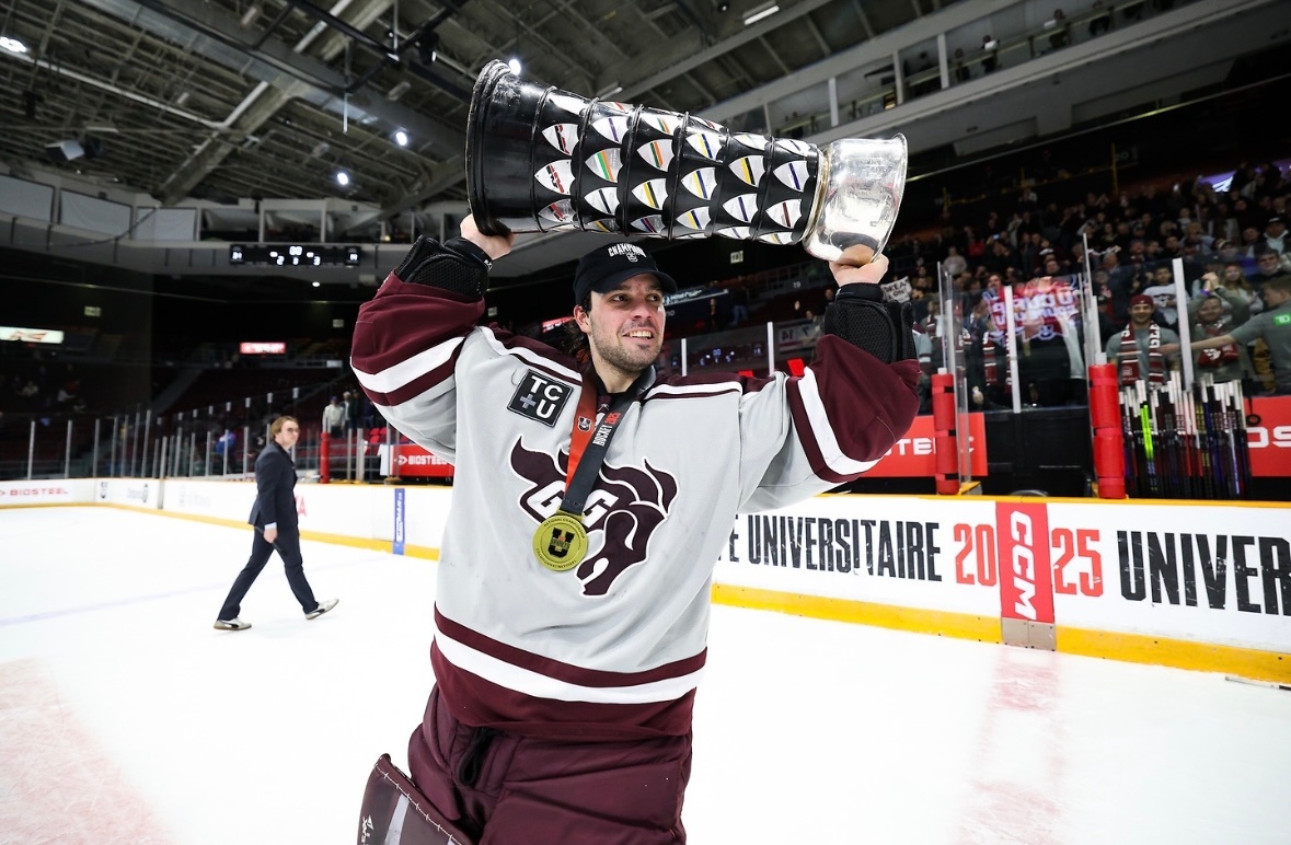Franky Lapenna skates, smiling as he lifts a large championship trophy while wearing the Gee-Gees’ grey and garnet uniform.