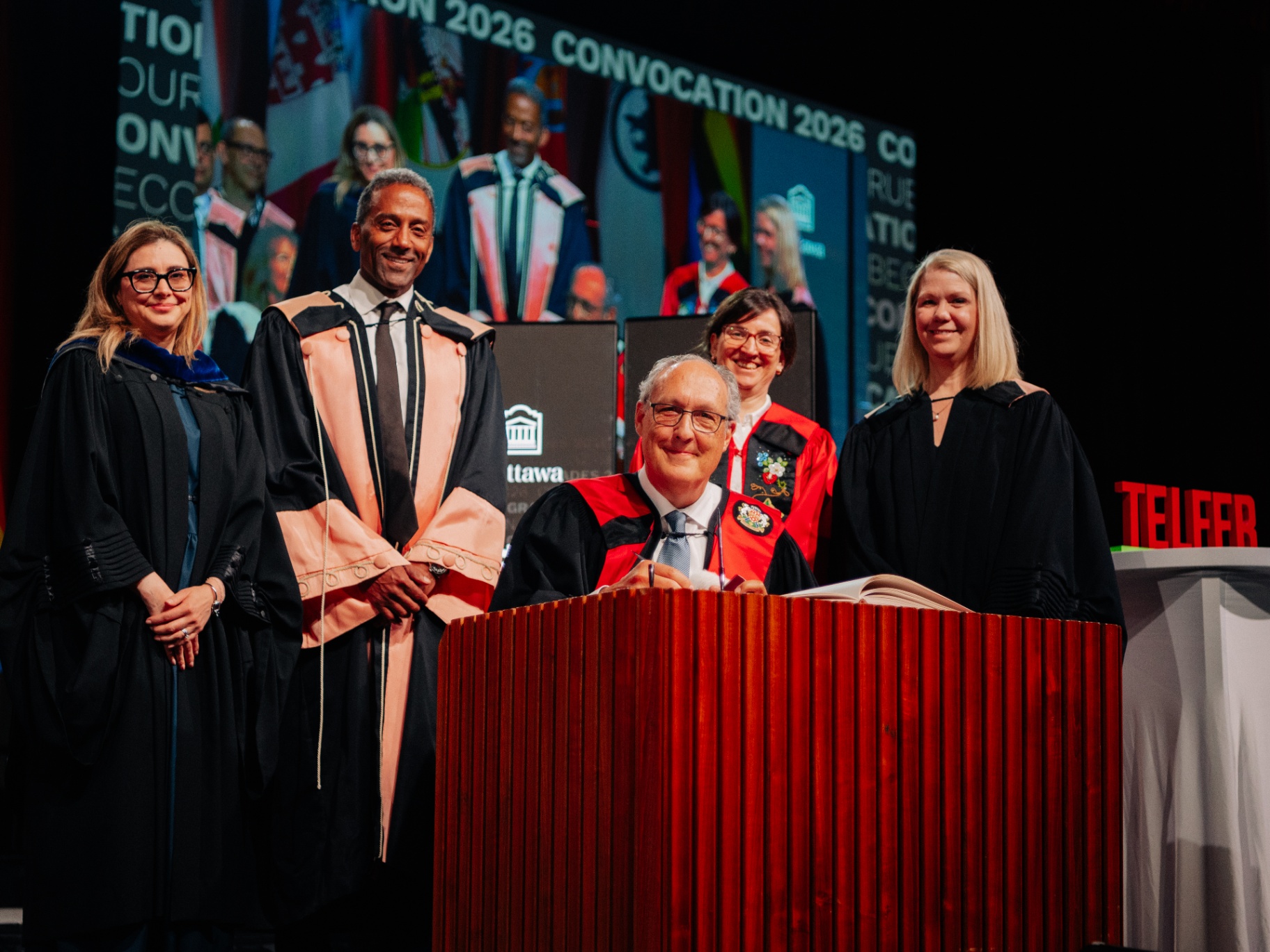 Professor Silvia Bonaccio, Dean Stéphane Brutus, Telfer alumnus Louis Gagnon, President and Vice-Chancellor Marie-Eve Sylvestre, and Doreen Hume are on stage in academic regalia during the University of Ottawa's 2026 convocation ceremony.