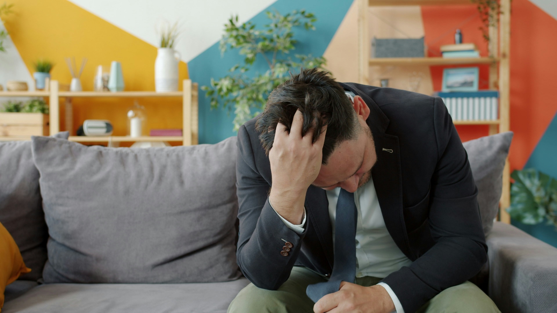 Homme sous l'effet du stress portant un complet et assis sur un divan gris