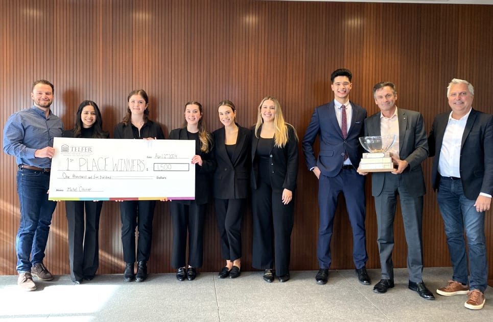 Myron Tetreault stands beside a group of students in business attire holding a cheque and a trophy.