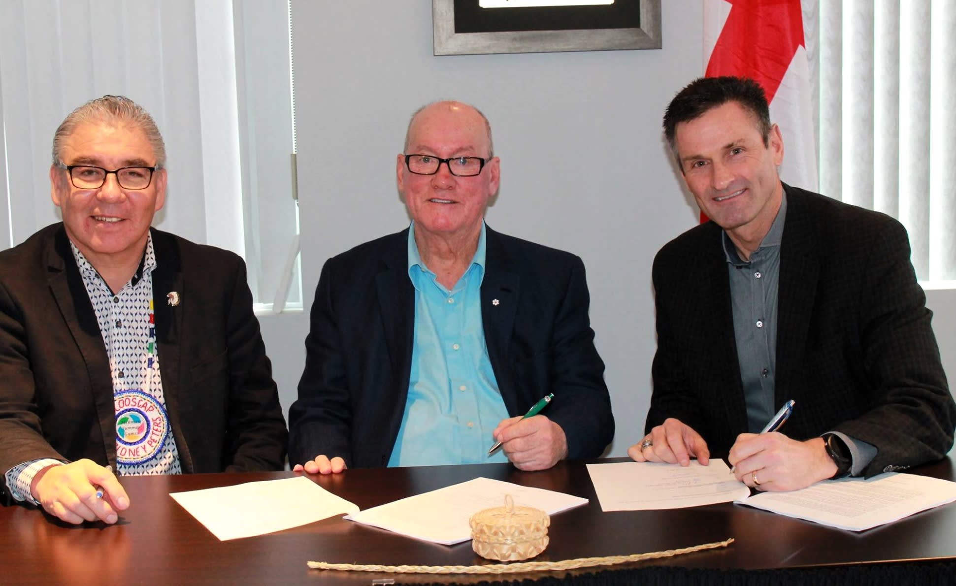 Myron Tetreault and two men in suits, seated at a table engaged in signing documents while smiling at the camera.