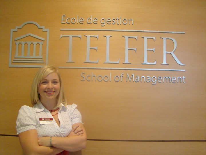 Amanda Richardson smiles for a photo with her arms crossed beside the Telfer logo.