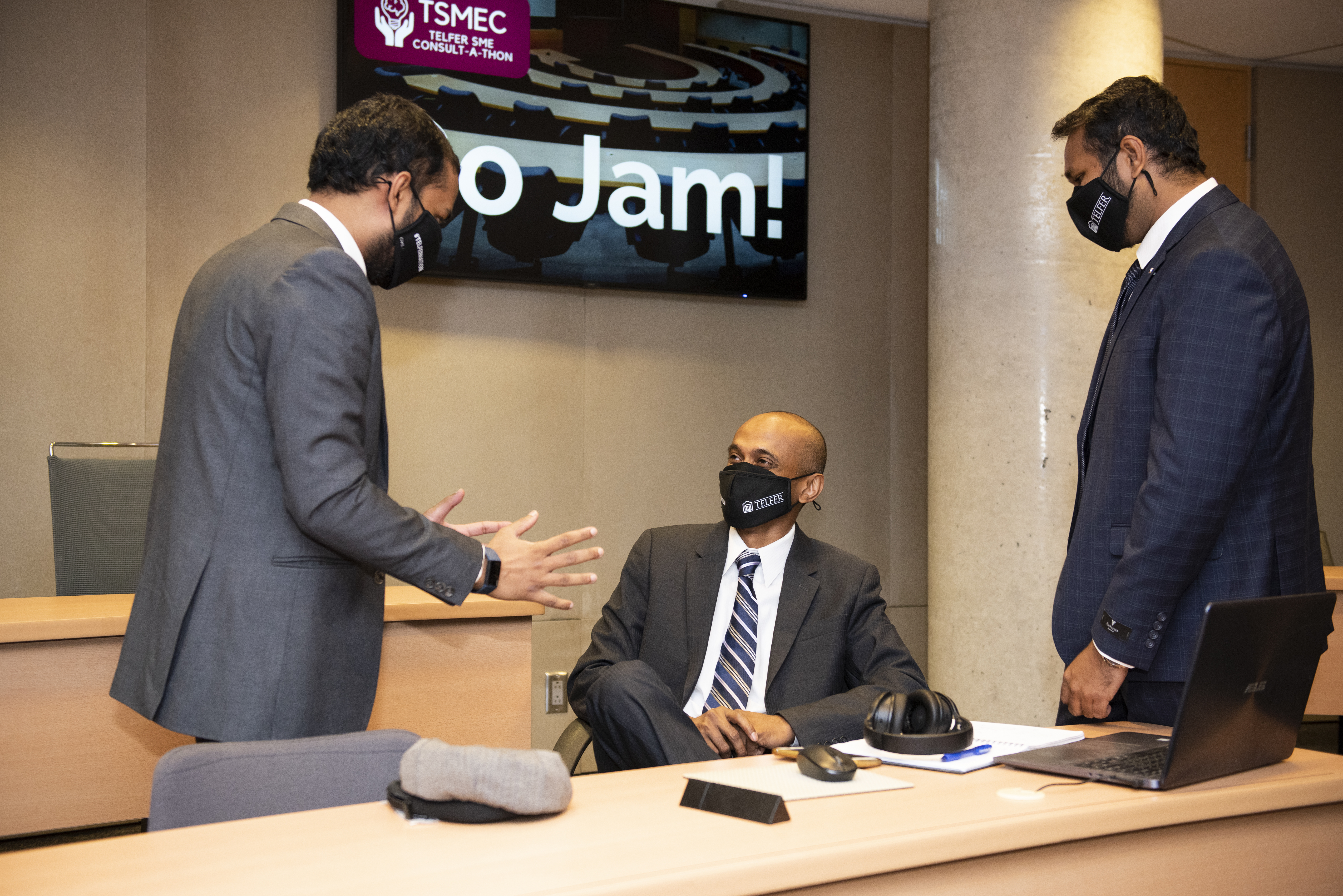 3 Businessman talking to each other around computers in a large classroom wearing masks