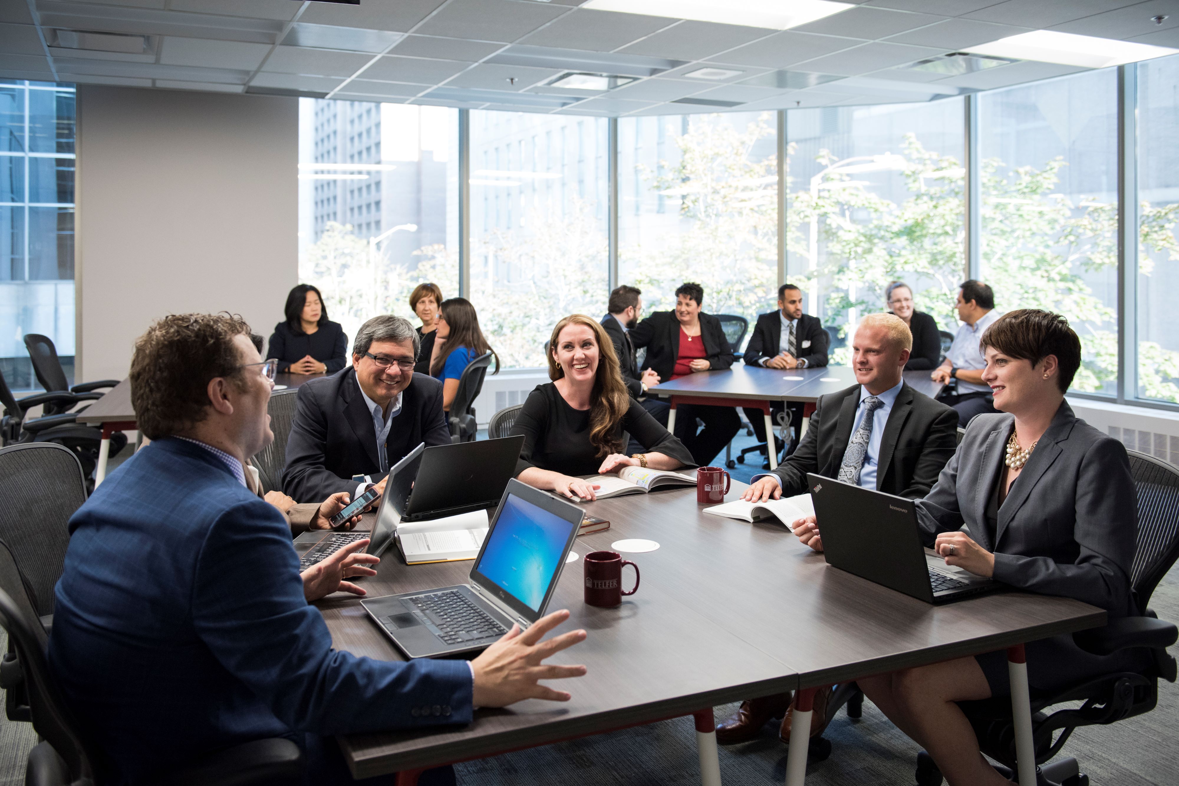 A group of diverse and well dressed Executive MBA students sit around a conference table for a meeting 