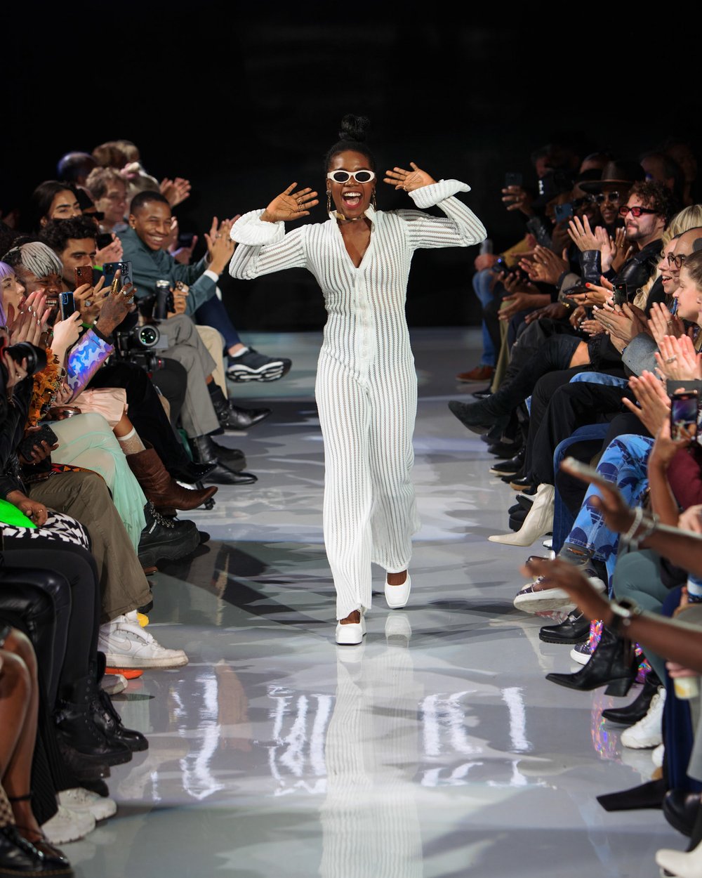 A model walking down the catwalk at a fashion show. She is wearing a white bodysuit designed by Chizoba Martin.