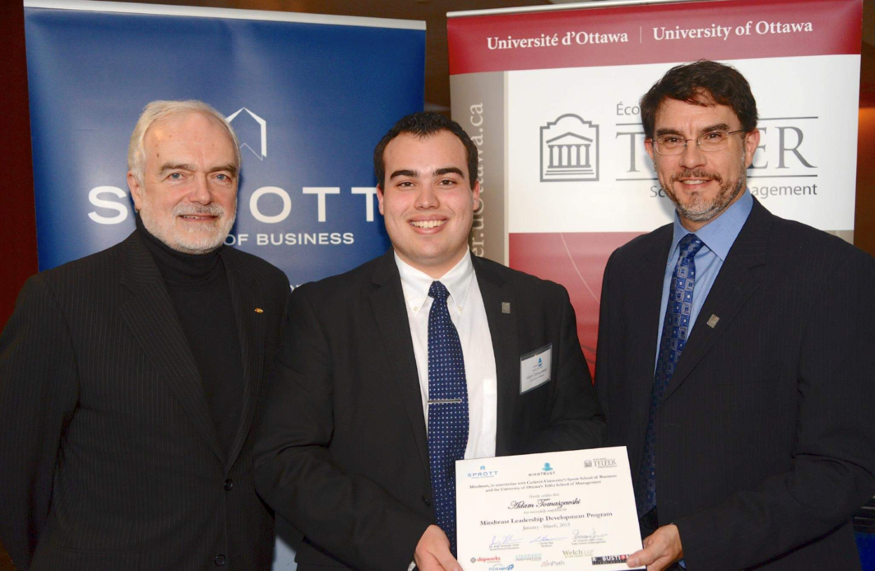 Adam Tomaszewski holding his diploma with Dean François Julien and another person