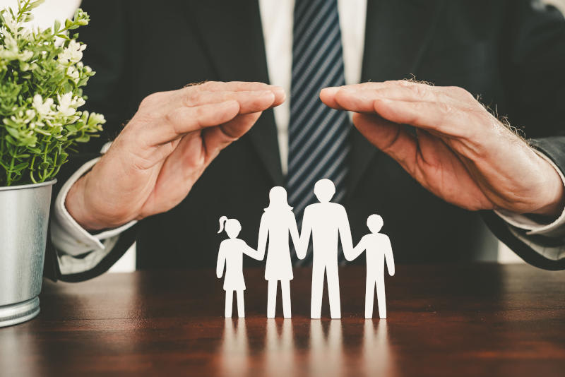 A person in a business suit holds their hands in a protective way over a paper cut out of a family of four holding hands