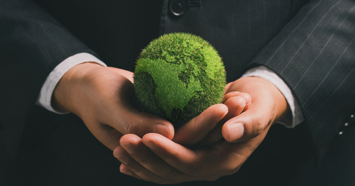 Business man holding small earth covered in grass.
