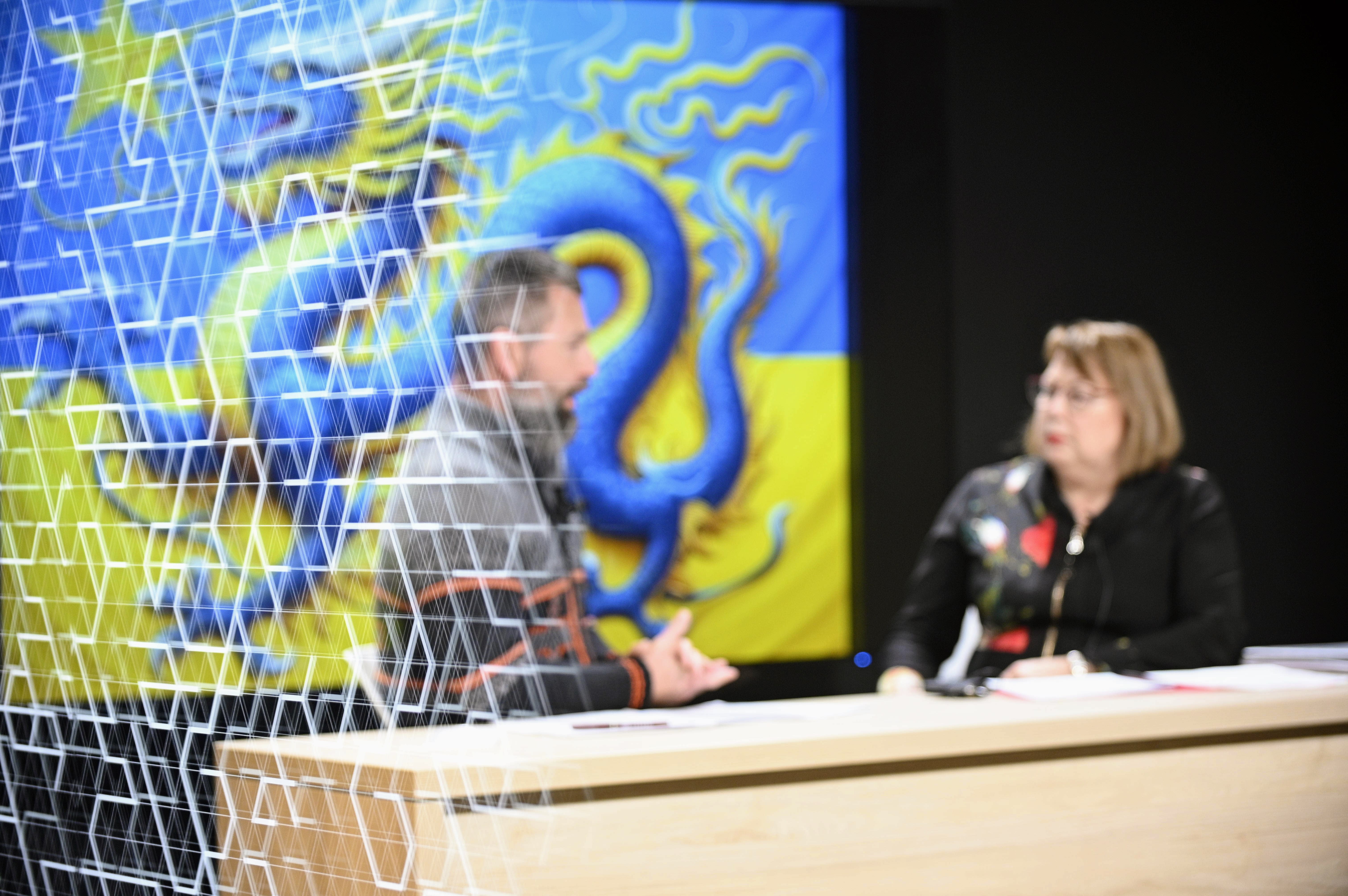 Two people are visible through a window, speaking to each other at a news desk at the uOttawa-IBM Cyber Range.