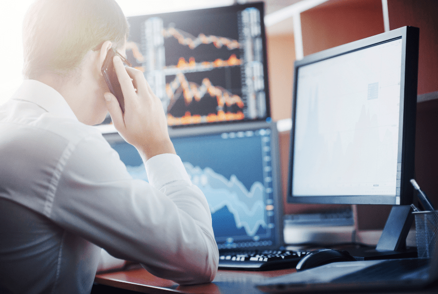 A fund manager looks at financial data on three screens while talking on the phone.