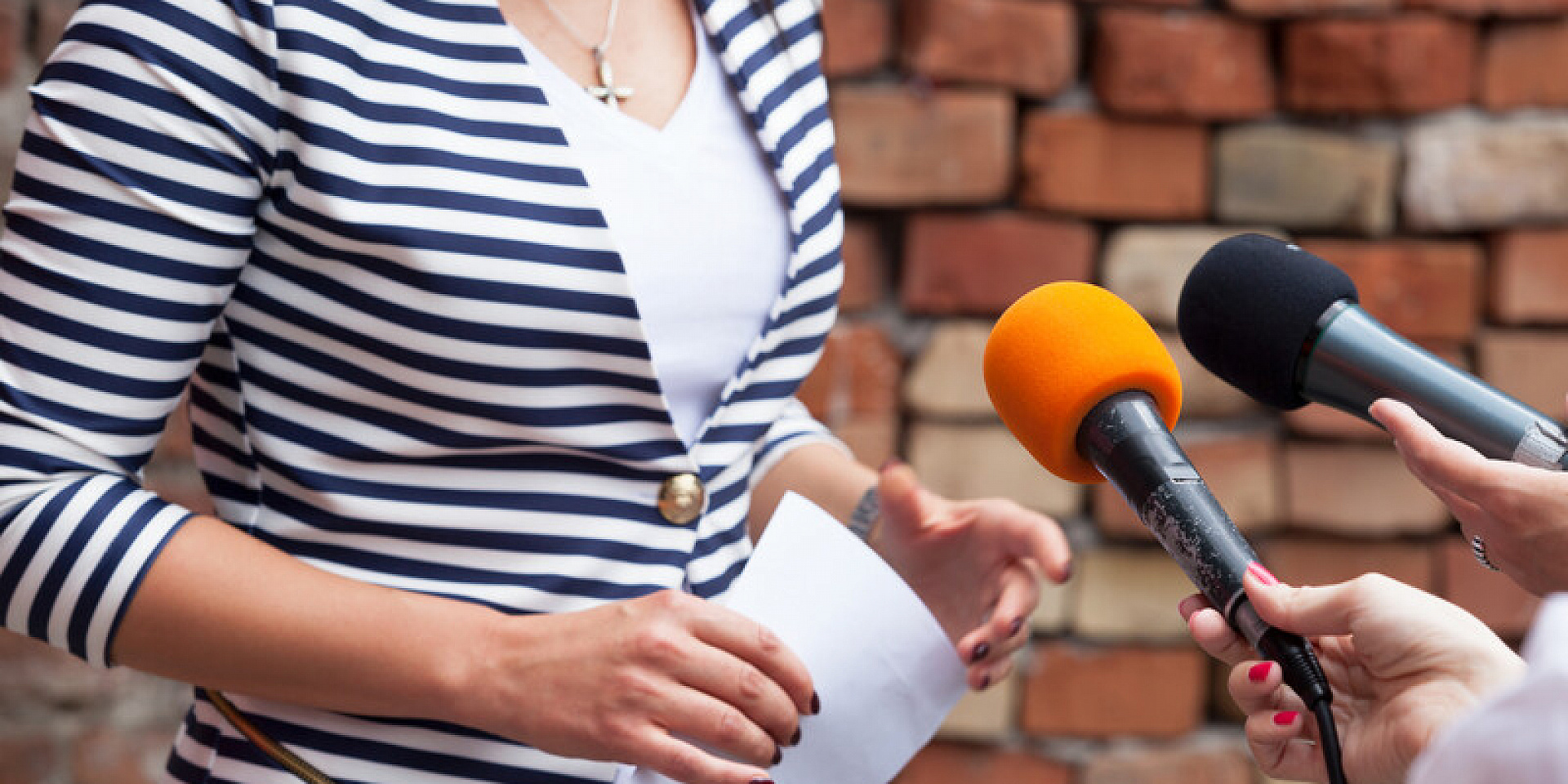 Women in a striped shirt talking into a black and a orange microphone