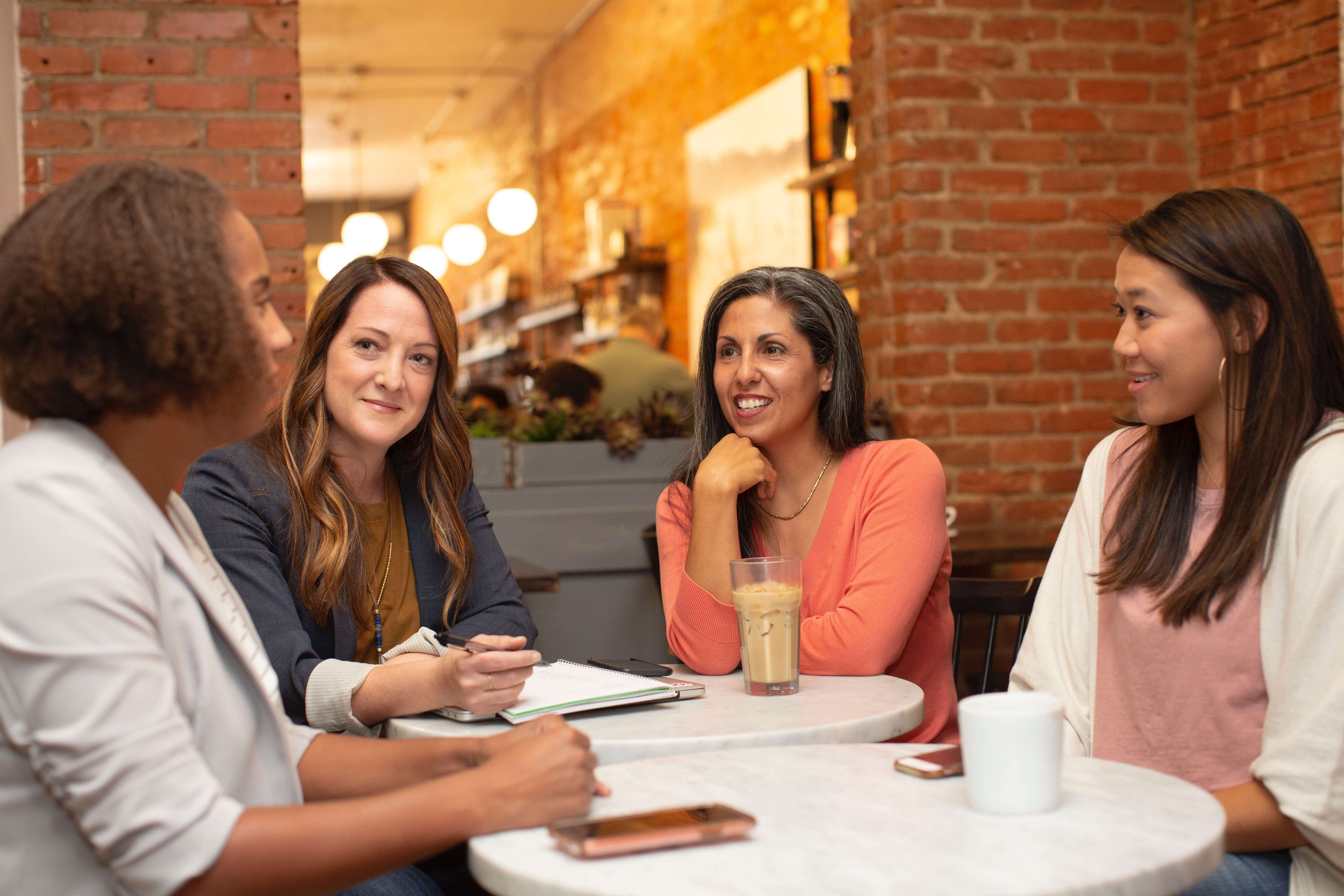 Four women are seated around a table and chat with one another.