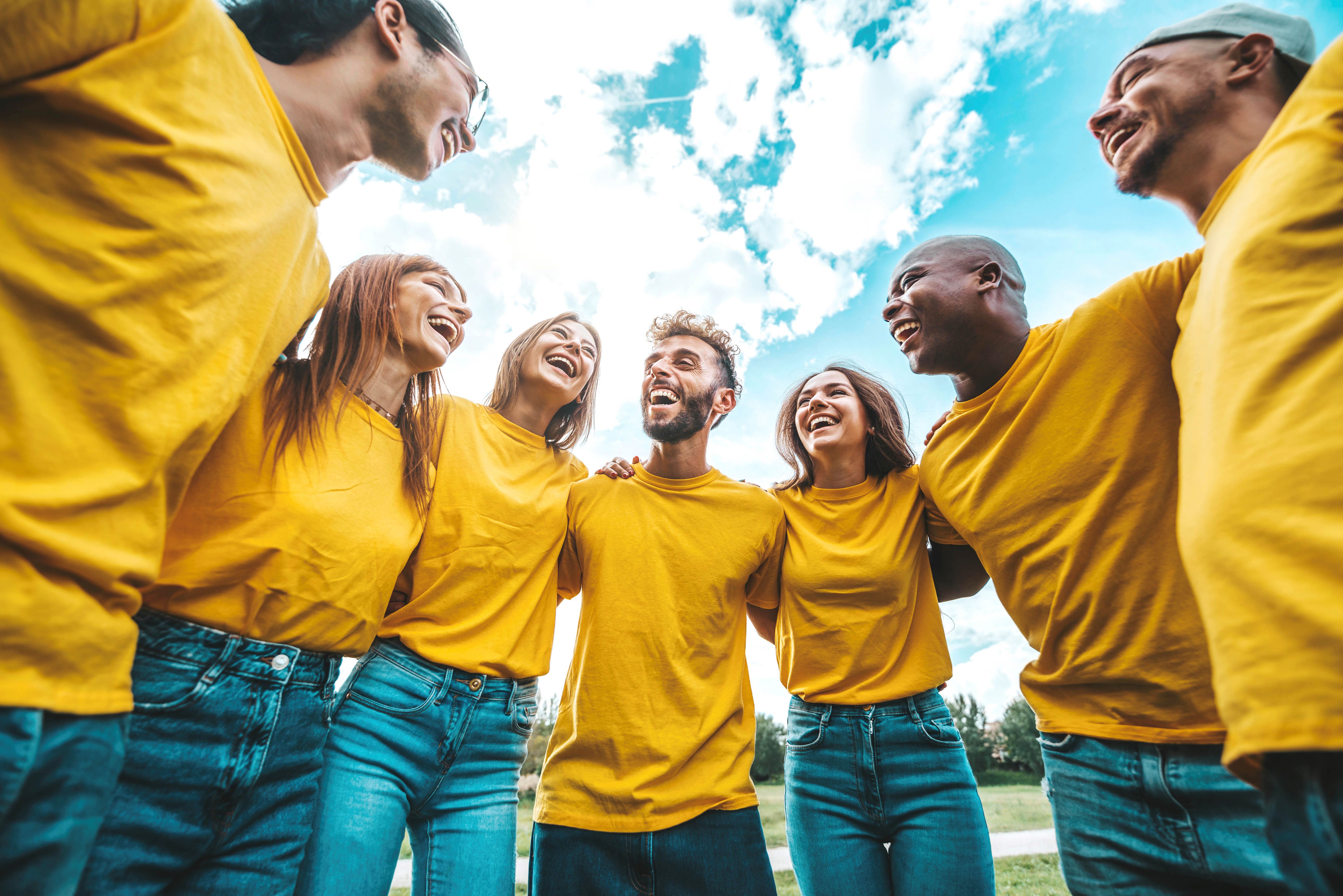 Group of people wearing yellow t-shirts hugging outside