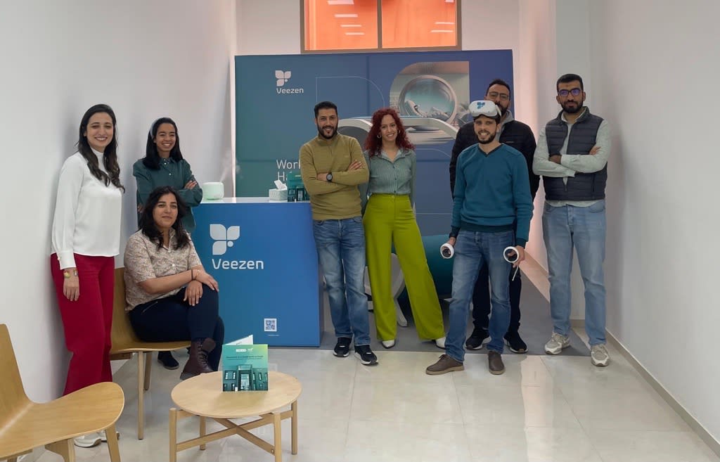 Group of eight people posing at Veezen booth with VR equipment and branding backdrop.