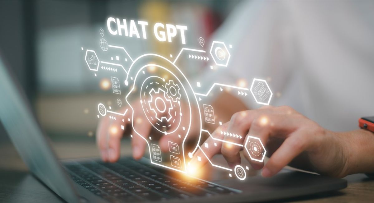 Image of fingers typing on a PC, with a ChaptGPT hologram of a head connecting to different hexagones.