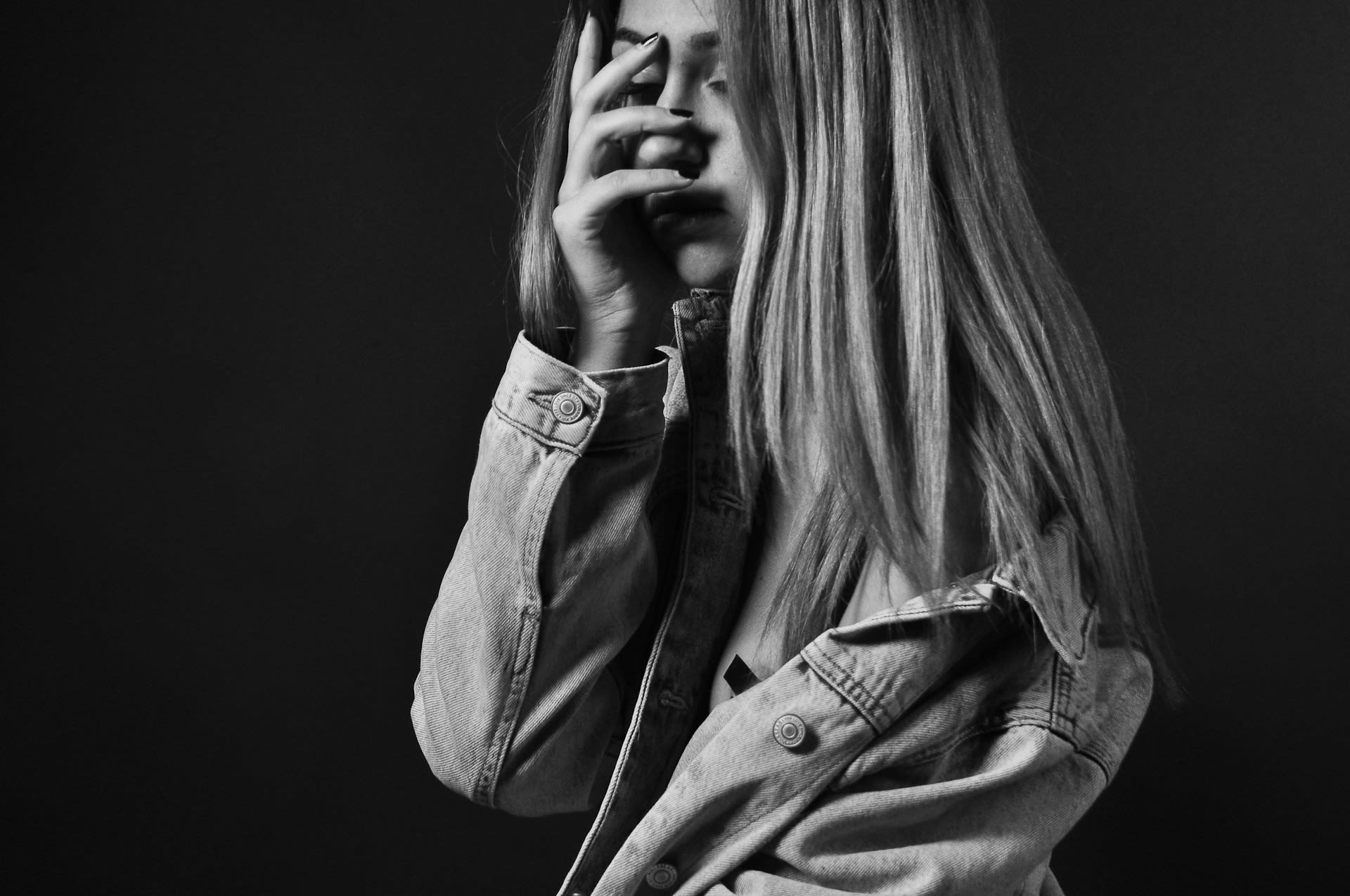 Person with long hair hiding their face with their hand