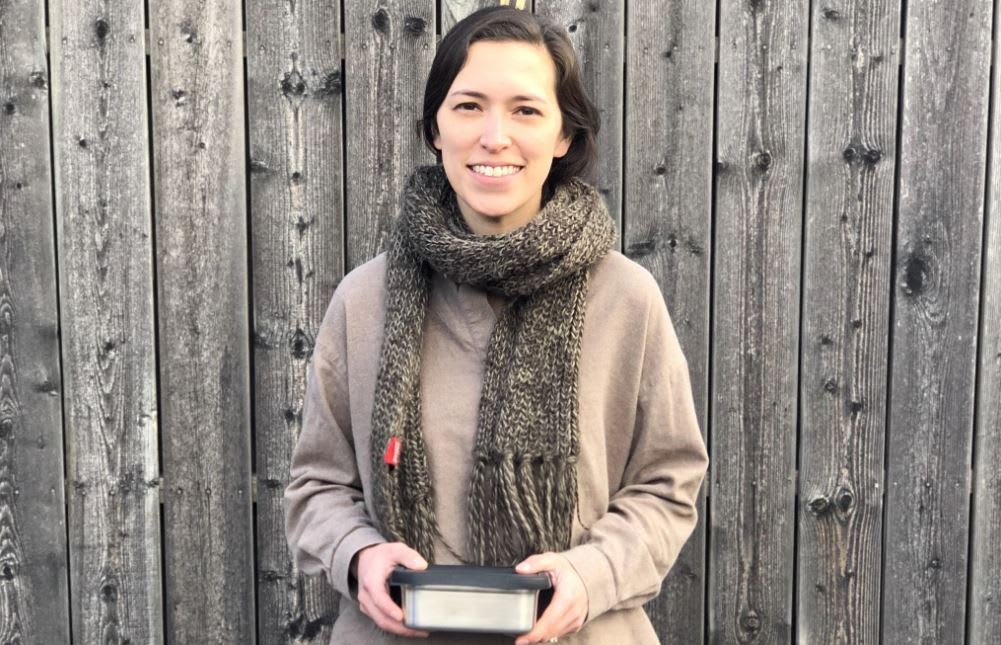Megan in front of a wooden fence holding a Suppli container.