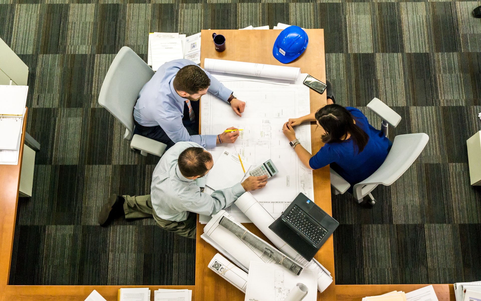 Overhead view of three people seated at a table reviewing a design