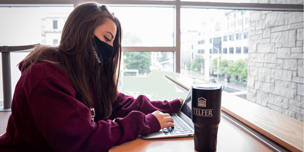 Student completing coursework on her laptop in the Desmarais Building