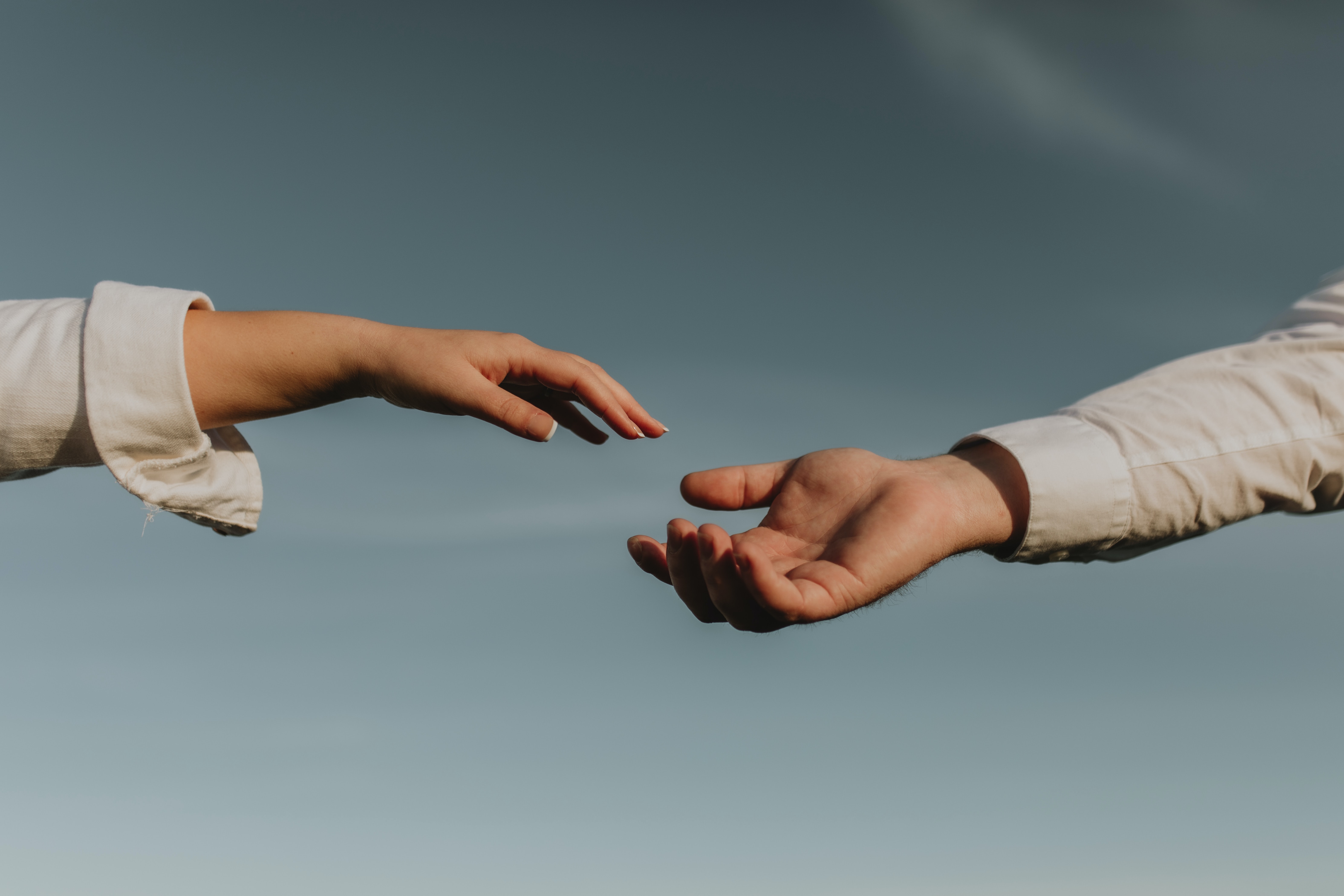 Two hands reaching toward one another with the sky in the background