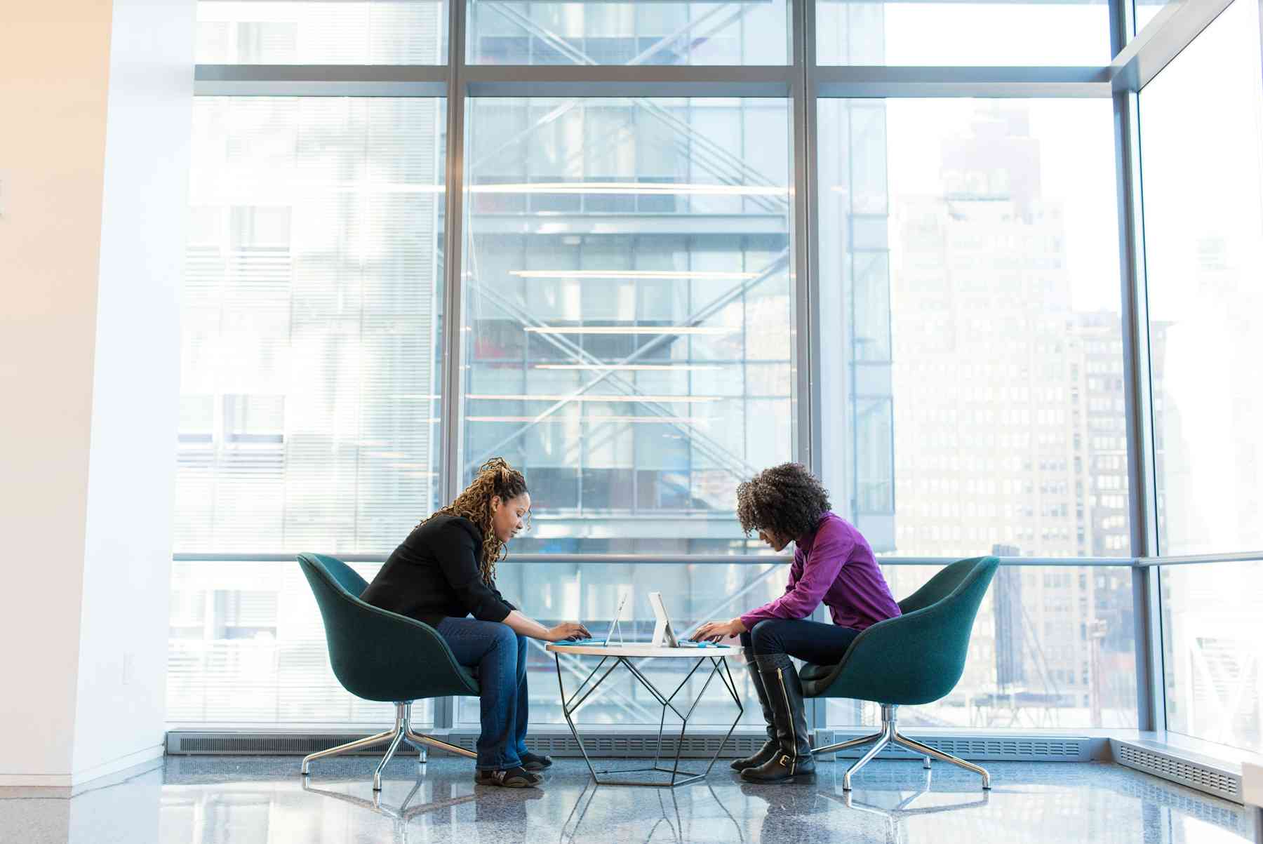 two women sitting across from each other and using their computers