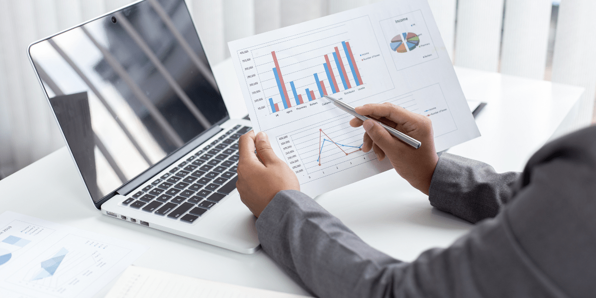 A person sitting in front of a computer looking at graphs printed on paper