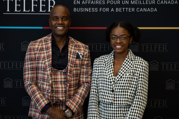 Wes hall and a Telfer student, both wearing plaid blazers, posing in front of a Telfer banner